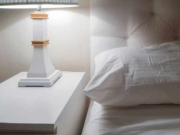 Luxe modern design van een lichte slaapkamer met een nachtkastje en een nachtlampje en een kussen op het bed, voorbereiding voor bed. - Foto, afbeelding