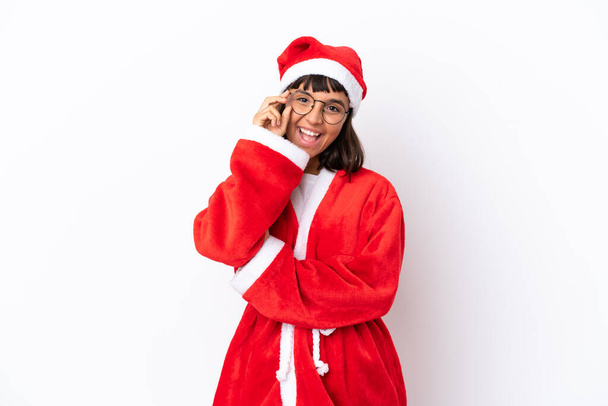 Młoda mieszana rasa kobieta przebrany za Świętego Mikołaja odizolowany na białym tle z okularami i szczęśliwy - Zdjęcie, obraz