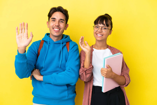 Junges Studentenpaar auf gelbem Hintergrund salutiert mit fröhlicher Miene an der Hand - Foto, Bild