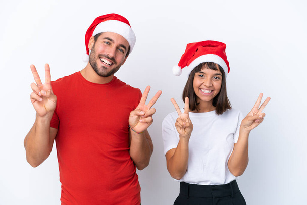 Молодая пара в рождественской шляпе на белом фоне улыбается и показывает знак победы обеими руками - Фото, изображение