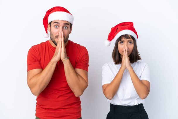 Νεαρό ζευγάρι με χριστουγεννιάτικο καπέλο απομονωμένο σε λευκό φόντο κρατά την παλάμη μαζί. Κάποιος ζητάει κάτι. - Φωτογραφία, εικόνα