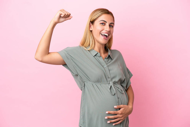Young Uruguayan woman isolated on blue background pregnant and doing strong gesture - Photo, Image
