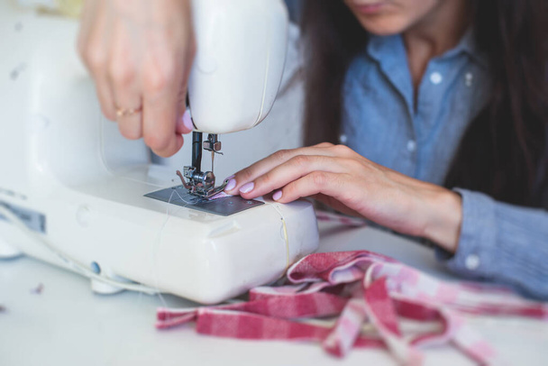 Process of hemming the dress and pants at home, close up of cloth on the sewing machine, hemming, tailoring, repairing and stitching cloth and dress, with the hand of female dressmaker  - 写真・画像