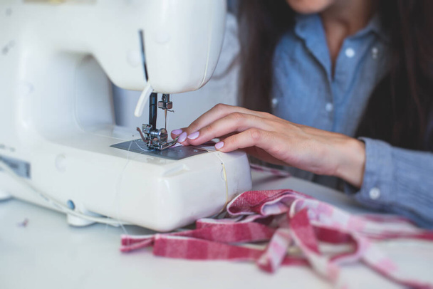 Process of hemming the dress and pants at home, close up of cloth on the sewing machine, hemming, tailoring, repairing and stitching cloth and dress, with the hand of female dressmaker  - Фото, изображение