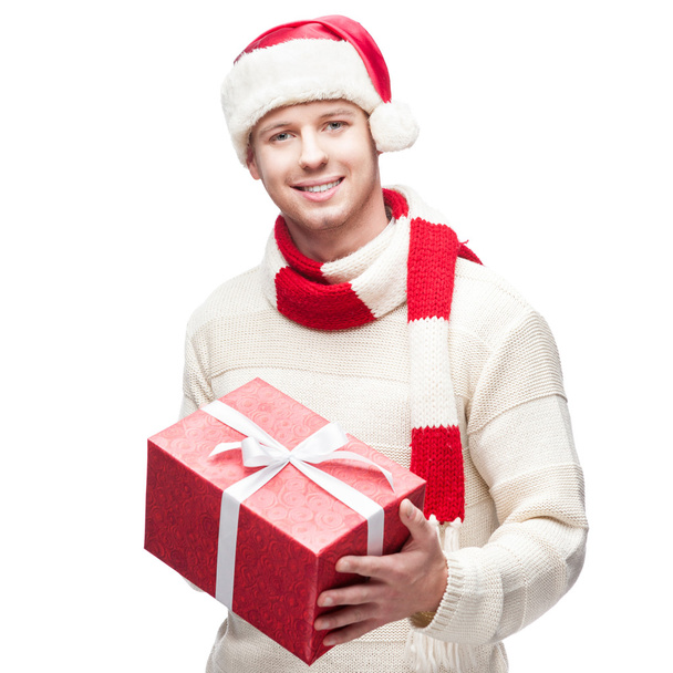 young casual man in santa hat hoding christmas gift - Zdjęcie, obraz