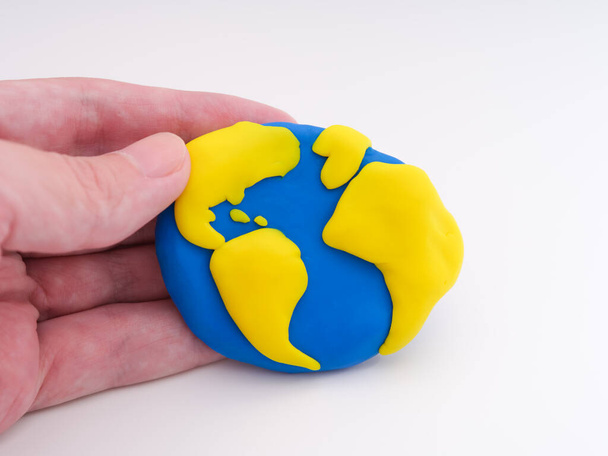 A man holding the planet Earth in his hand. The planet Earth is made out of polymer clay. - Fotó, kép