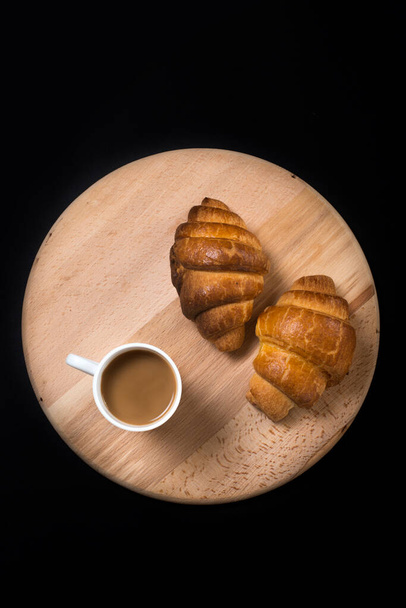 From above view of two fresh croissants and  mug with coffee placed on napkin on black background of table - Foto, Imagem