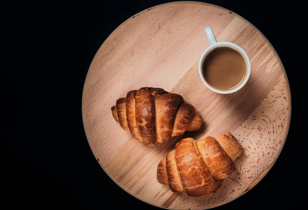 From above view of two fresh croissants and  mug with coffee placed on napkin on black background of table - Foto, Bild