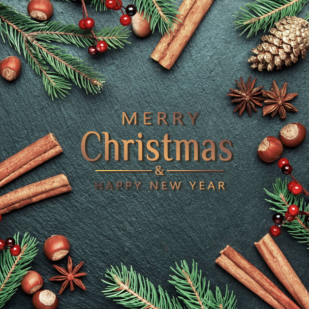 Merry Christmas and Happy New Year dark background with text. Frame, template with festive decorations, winter spices, nuts and fir branches, top view - 写真・画像