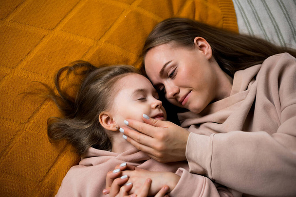 mom is lying on the bed and stroking her daughter's cheek - 写真・画像