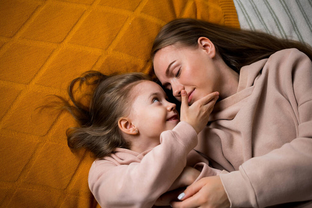 la fille se couche sur une couverture sur le lit et caresse sa mère sur la joue - Photo, image