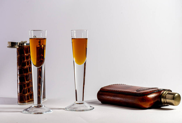 dva sáčky pro uchovávání obecně alkoholických nápojů a dvě sklenice obsahující opékanou tekutinu na lehkém podkladu - Fotografie, Obrázek