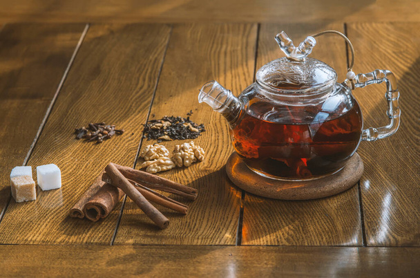Hot spiced tea with cinnamon in glass teapot on wooden background - Фото, зображення