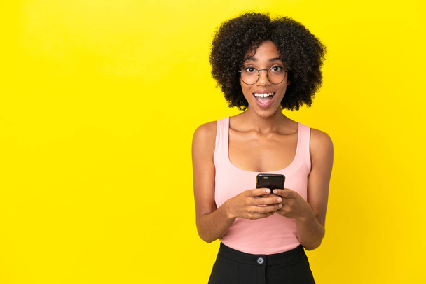 Молодая афроамериканка, изолированная на желтом фоне, удивлена и отправляет сообщение - Фото, изображение