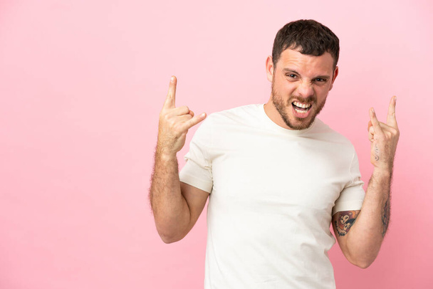 Young Brazilian man isolated on pink background making horn gesture - Foto, imagen