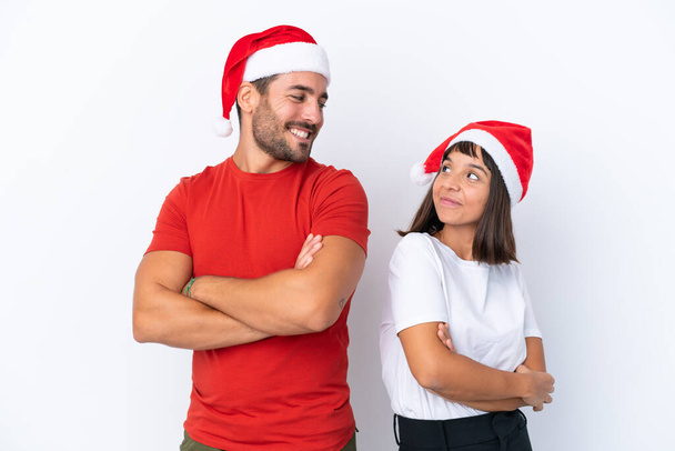 Fiatal pár karácsonyi kalap elszigetelt fehér háttér néz a válla fölött egy mosollyal - Fotó, kép