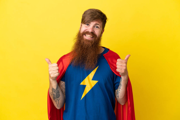 Redhead Super Hero man isolated on yellow background with thumbs up gesture and smiling - Photo, Image