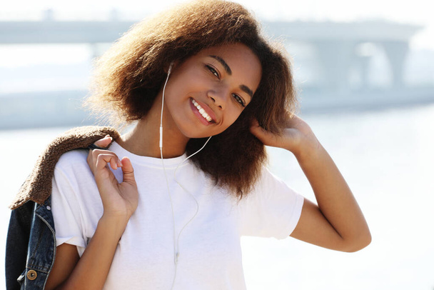 lifestyle concept: Young african american girl using mobile phone and headphones, smiling, close up - Foto, immagini