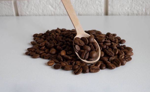 Granos de café aromáticos en una cuchara de madera, granos de café para la producción de delicioso café. granos de café enteros para moler. - Foto, Imagen