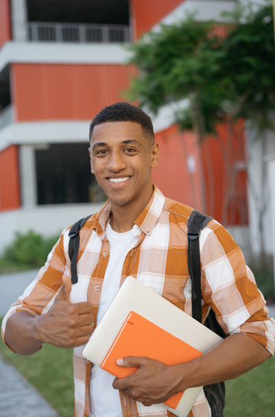 Ritratto di successo sorridente studente afroamericano tenendo pollice in su guardando la fotocamera in piedi nel campus universitario - Foto, immagini