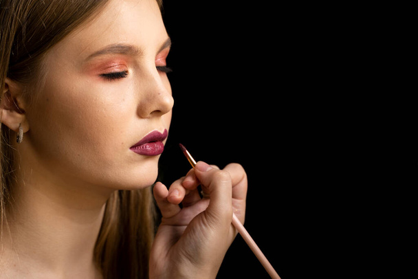 Makeup artist applies red lipstick on a beautiful woman face. Hand of make-up master, painting lips of young beauty model girl. Make up in process. - Fotografie, Obrázek