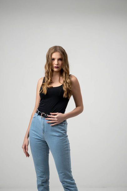 Beautiful young woman portrait in a black t-shirt and blue jeans. Studio shot, isolated on gray background. - Photo, image