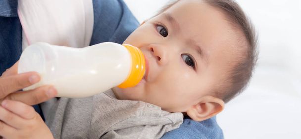 Młoda azjatycka matka obejmująca i karmiąca małą dziewczynkę butelką mleka w domu, nowo narodzona niewinność pijąca z zadowoloną mamą, związek i więź mamy z dzieckiem, koncepcja rodziny. - Zdjęcie, obraz