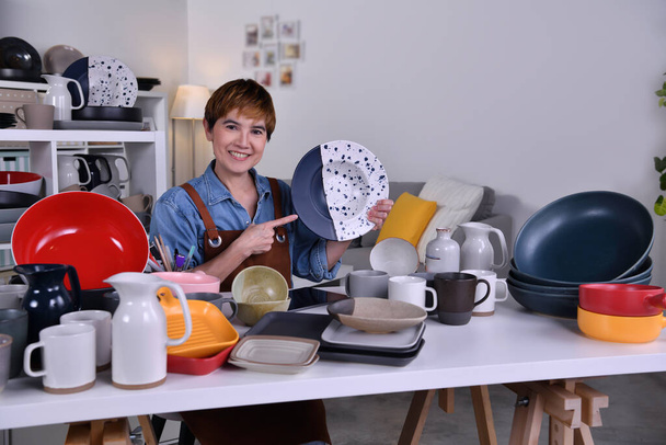 Зріла азіатська жінка-підприємець / діловий власник показує свій глиняний керамічний продукт і працює вдома. - Фото, зображення
