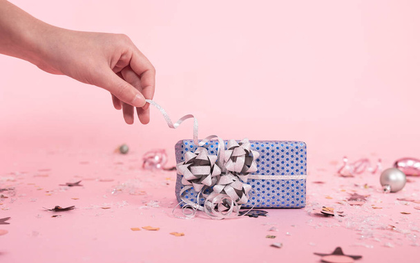 Weihnachten rosa Hintergrund mit einem Geschenk, die Hand einer Frau packt das Geschenk aus, zieht das Band. - Foto, Bild
