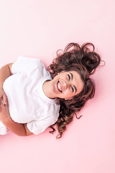 Atrakcyjna brunetka w białej koszulce uśmiecha się na różowym tle. - Zdjęcie, obraz