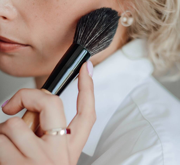 Make-up-Pinsel in der Hand einer Frau in der Nähe des Gesichts - Foto, Bild