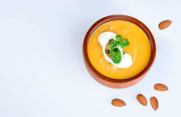 yellow pumpkin soup served and ready with bread, two pieces of raw pumkin in the background, thanksgiving or winter meal, traditional autumn food - Photo, Image