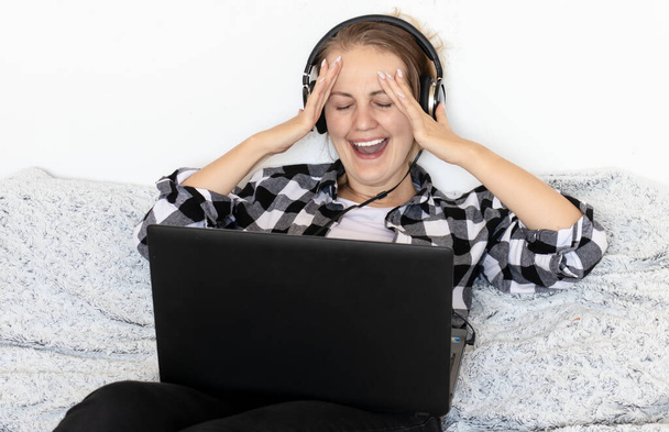 Ein junges Mädchen schaut auf einem Laptop mit Kopfhörern einen Film. auf dem Bett sitzend - Foto, Bild