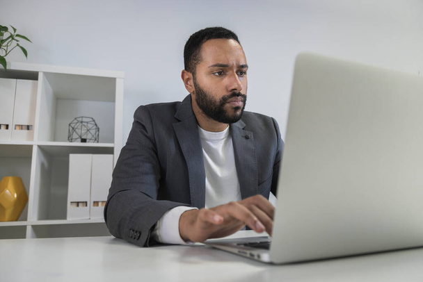 Jonge Afro-Amerikaanse zakenman werkt op laptop in het thuiskantoor. Gericht ondernemer typen op zijn computer. - Foto, afbeelding