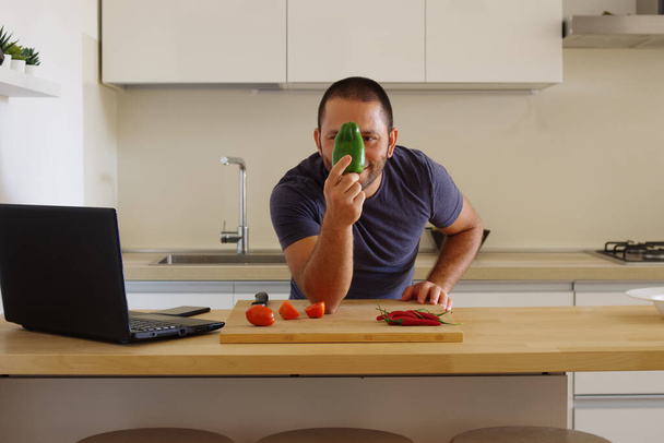 A white man looking at a paprika in front of vegetables on a board in the kitchen - Foto, afbeelding
