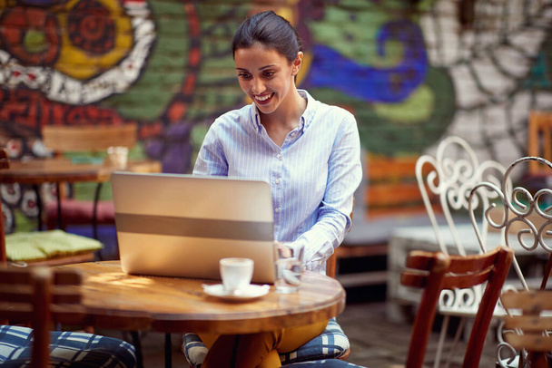 young adult caucasian female sitting in the outdoor cafe looking at her laptop, smiling - Photo, Image