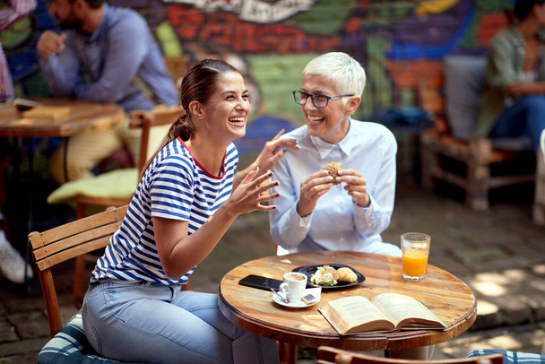 elderly and young adult women laughing at outdoor cafe, having breakfast and a wonderful time. different age female friends relationship concept. - Zdjęcie, obraz