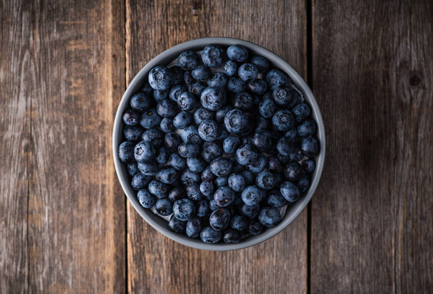 Blueberries in ceramic bowl on rustic wooden background. Selective focus. Shallow depth of field. - Photo, image