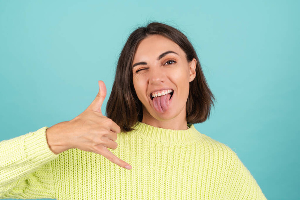 Young woman in light green sweater cute happy smiling shows phone gesture - Foto, immagini