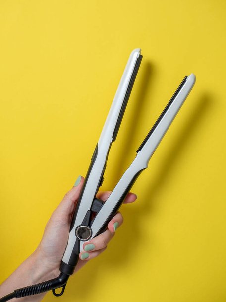White curling iron in a woman's hand on a yellow background. An accessory for creating hairstyles. Beauty and fashion. Hair care. - Photo, Image