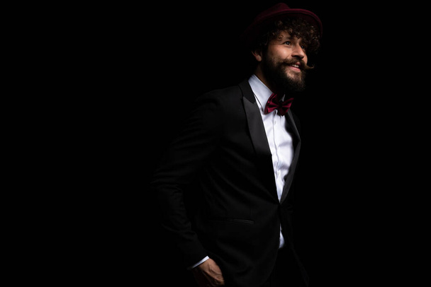 fiatal jóképű üzletember egyik kezét a zsebében tartva, burgundi kalapot visel és mosolyog  - Fotó, kép