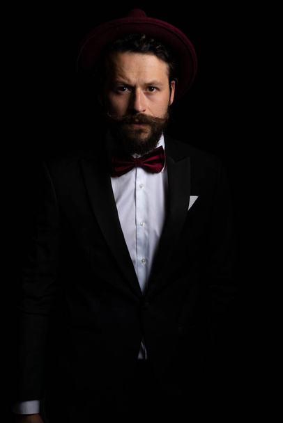 portrait of a handsome businessman wearing a burgundy hat and a nice tuxedo in a fashion pose - Photo, Image
