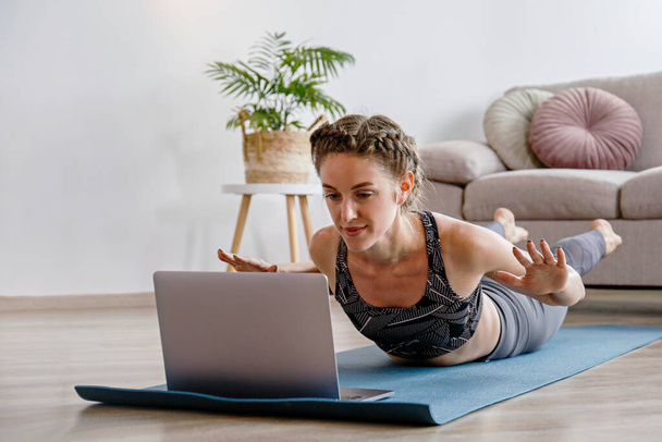 Jeune femme sportive enseignant le yoga en ligne dans le confort de sa propre maison. Yogini diffusion yoga en direct pose variation de la salle de séjour. Arrière-plan intérieur, espace de copie, gros plan. - Photo, image