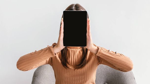 Jovem segurando tablet pc com tela em branco na frente de seu rosto no fundo branco, mockup para aplicativo ou site - Foto, Imagem