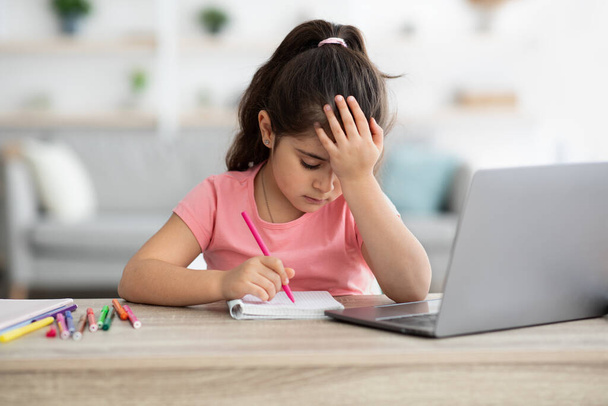 Otthoni tanulási nehézségek. A feldúlt kislány belefáradt a laptopos házi feladatba. - Fotó, kép