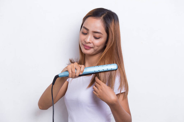 young asian beautiful happy woman straightening hair with hair straightener on white background - Photo, Image