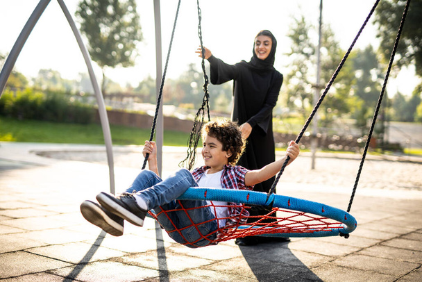 Cinematic image of a woman from the emirates with her children having fun at the playground - Zdjęcie, obraz