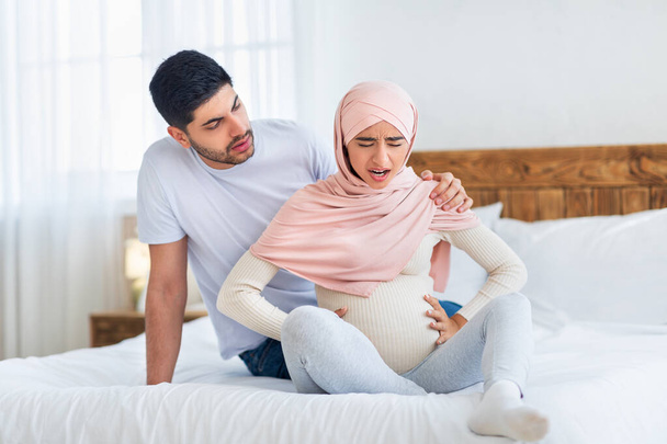 Беспокойный муж-араб, поддерживающий беременную жену предродовыми схватками, сидящий вместе на кровати, копирующий пространство - Фото, изображение