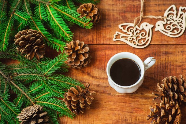 Christmas background. Spruce branches, wooden bird figures cones and cup with coffee on a wooden background. Copy space, frame, place for text. Top view. Christmas or New Year's card. flat lay - Photo, Image