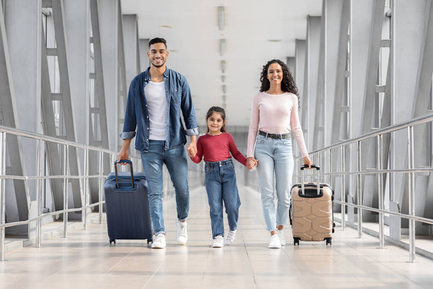 Listo para las vacaciones. Familia feliz de Oriente Medio caminando con maletas en la terminal del aeropuerto - Foto, imagen